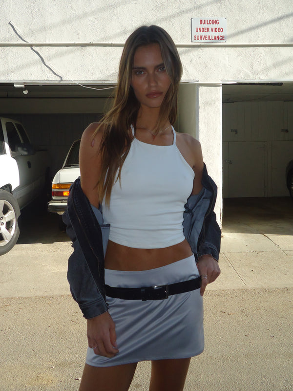 Modelo usando crop top crudo halter con mini falda y camisa negra.