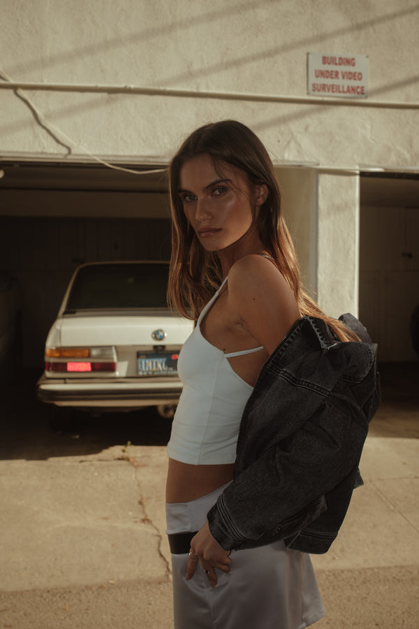 Vista lateral modelo con crop top tipo halter crudo, mini falda y chaaqueta.