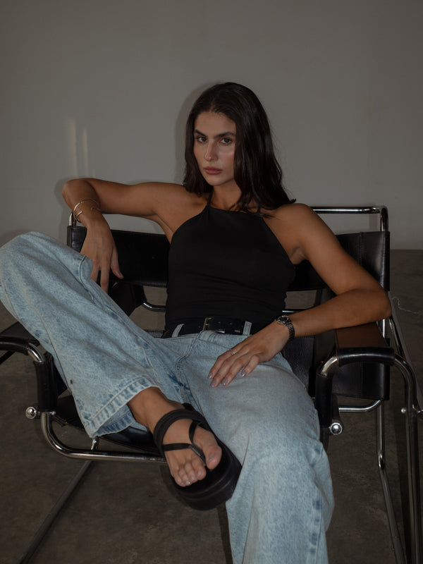 Modelo sentada usando crop top negro halter con jean y sandalias.