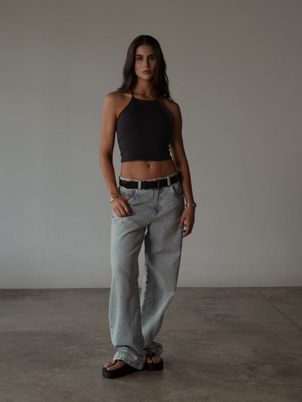 Modelo con jean clásico y crop top halter negro con sandalias y cinturón.