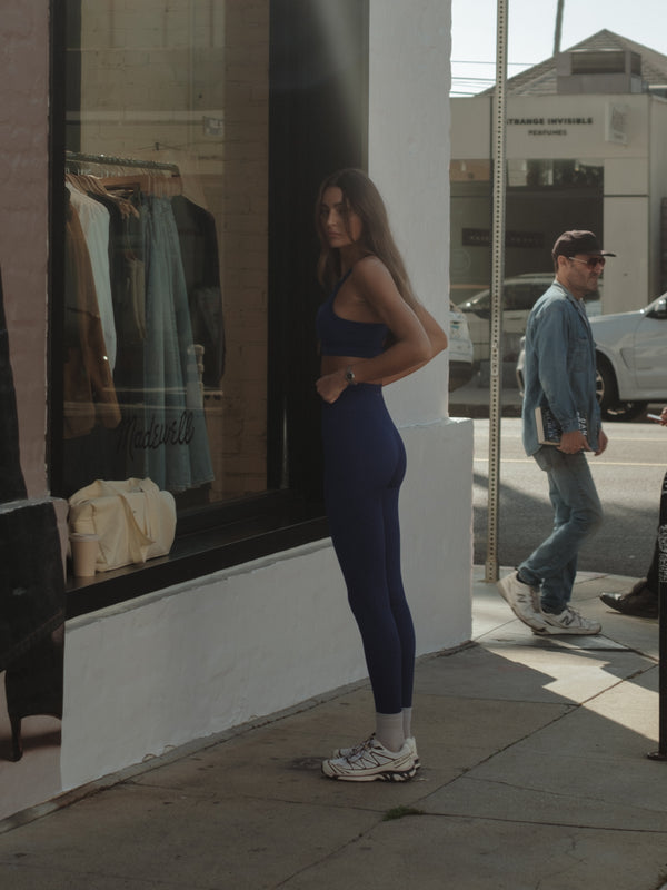 Modelo fuera de una tienda usando ropa deportiva púrpura y tenis.