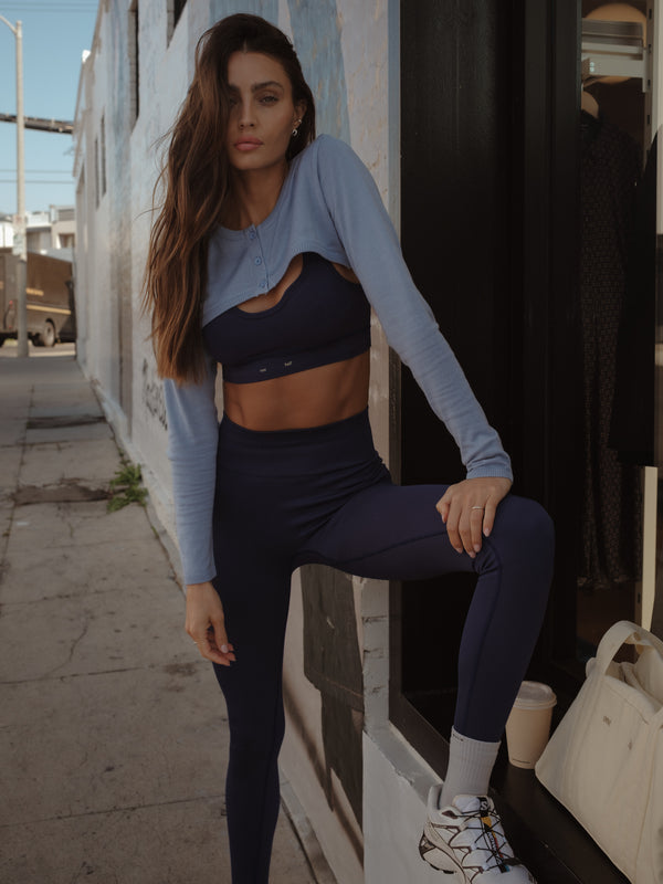 Modelo con mini cárdigan azul con set deportivo púrpura sin costuras.
