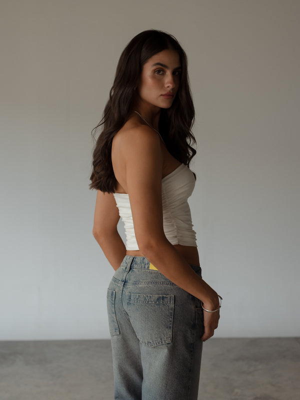 Vista posterior de modelo usando crop top crudo drapeado strapless. 