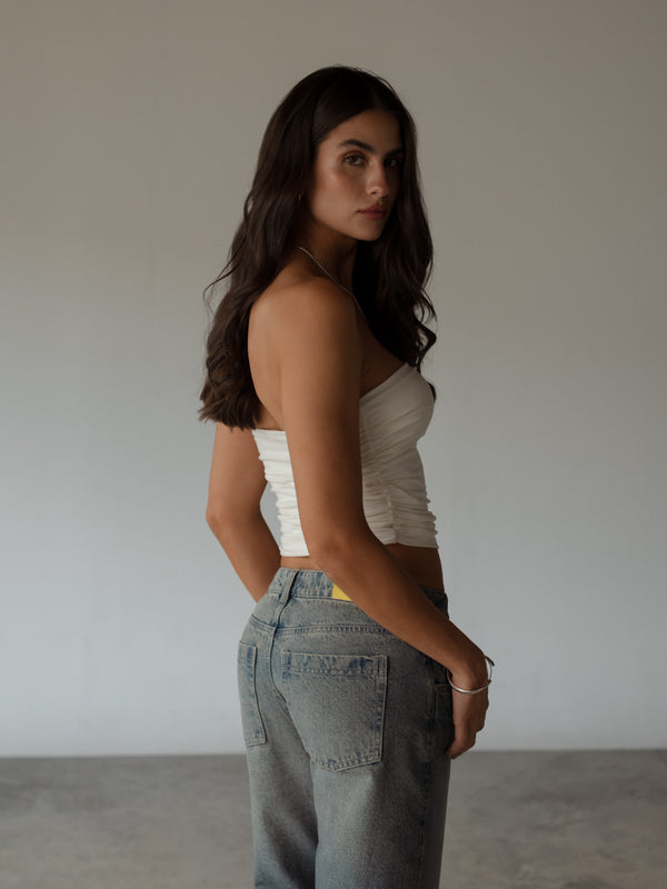 Vista posterior de modelo usando crop top crudo drapeado strapless. 