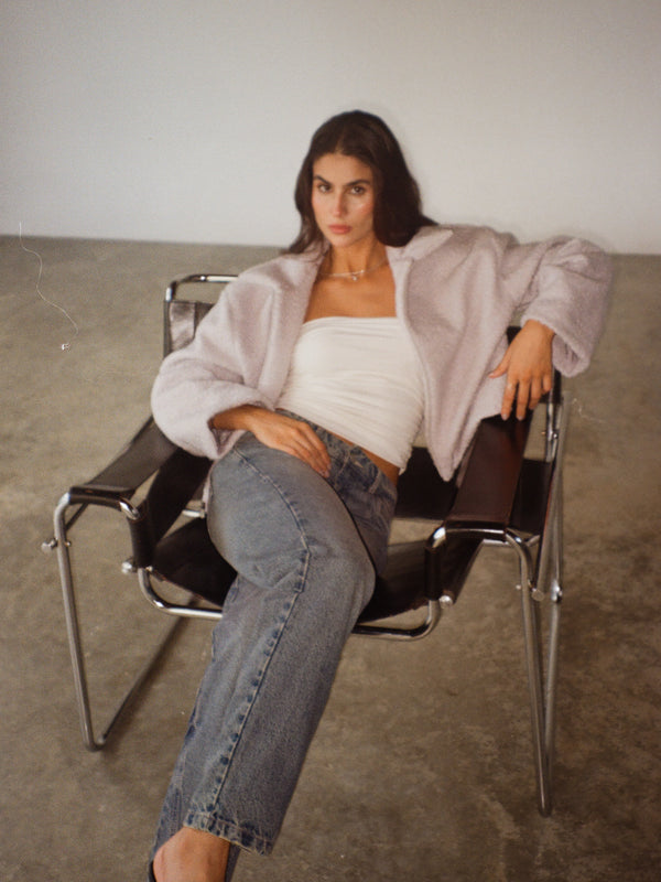 Modelo sentada usando crop top crudo con chaqueta y jean.