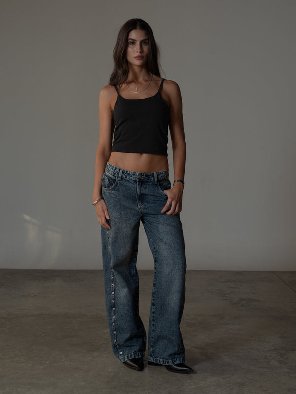 Modelo con crop top básico de tiras negro con jean azul y botas.