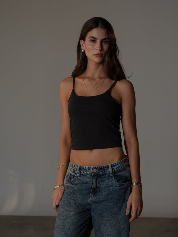 Vista frontal de modelo con crop top negro de tiras ajustado con jean azul.