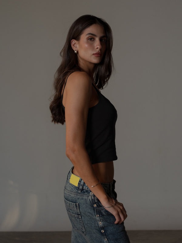 Vista lateral modelo con crop top negro de tiras básico con jean azul.