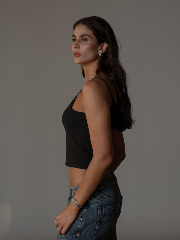 Vista lateral modelo usando jean azul con crop top básico negro de tiras.