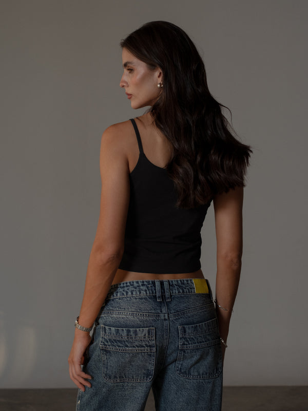 Vista posterior modelo usando crop top negro de tiras con jean azul.