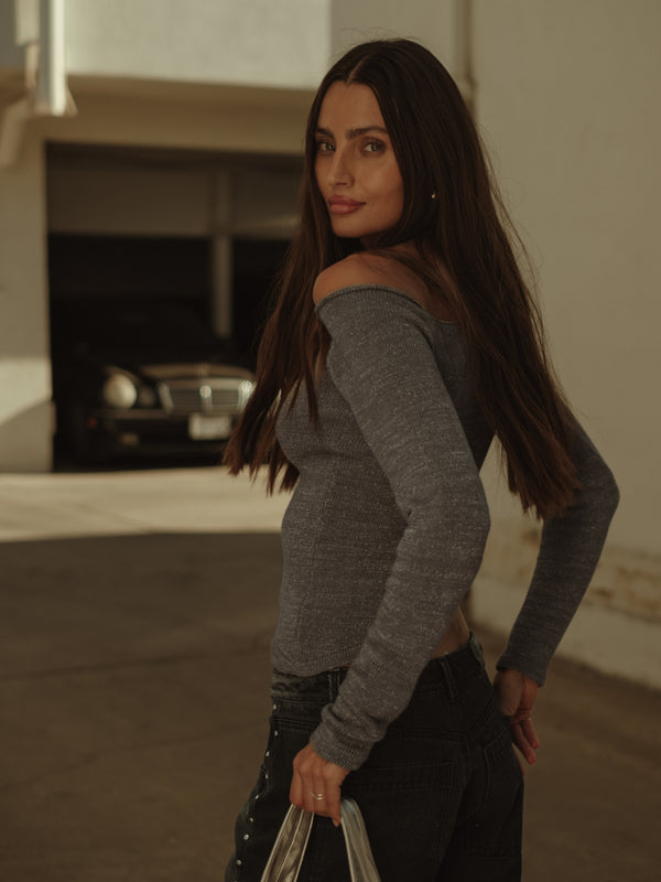 Vista posterior modelo con top tejido manga larga gris brillante asimétrico.