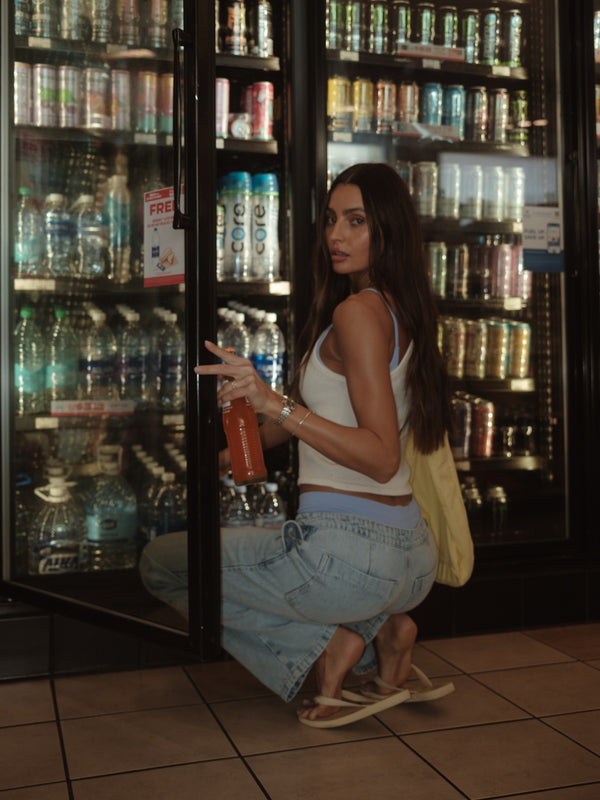 Modelo en tienda buscando un refresco usando top crudo y jean azul.