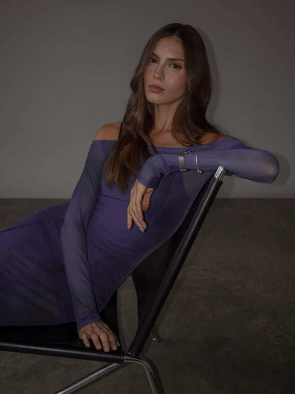 Modelo sentada usando vestido de hombros descubiertos púrpura.