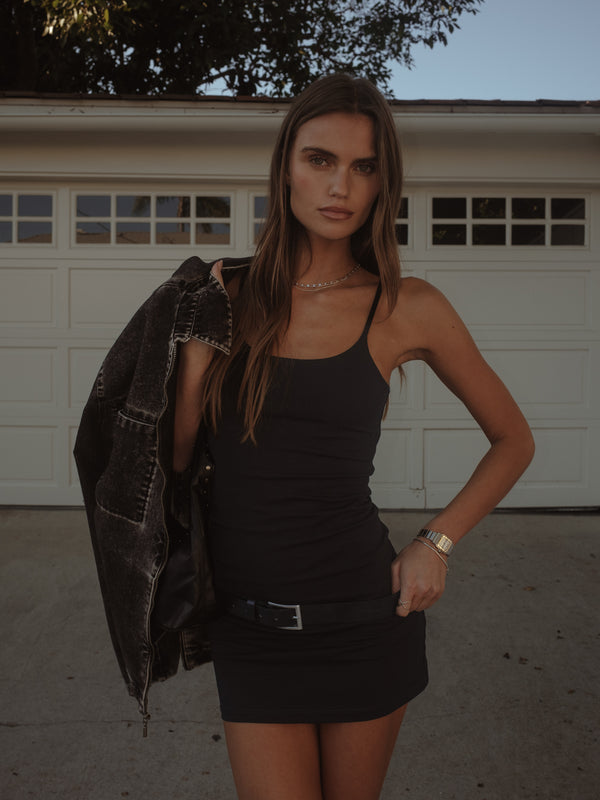 Modelo usando mini vestido negro de tiras con cinturón y chaqueta.