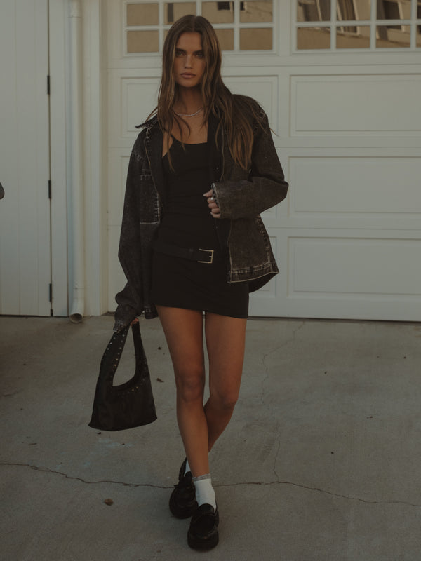 Modelo usando mini vestido negro, chaqueta negra oversized y bolso.