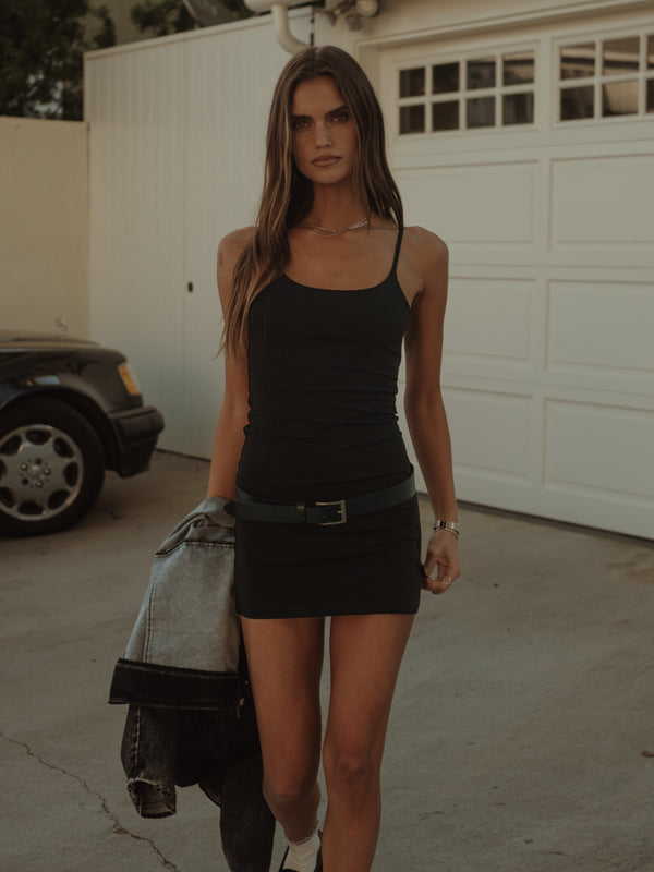 Modelo usando mini vestido negro de tiras, sosteniendo una chaqueta.