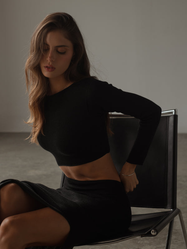 Modelo sentada usando vestido negro  tejido manga larga.