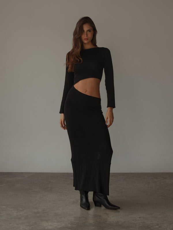 Modelo usando vestido negro tejido con abertura en el abdomen.